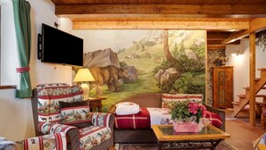 Un salon chaleureux avec une fresque murale, des meubles en bois, un téléviseur à écran plat et un escalier.