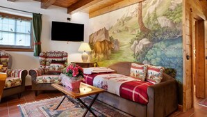Un salon chaleureux avec une grande fresque murale, un canapé, des fauteuils, une table basse et un téléviseur.