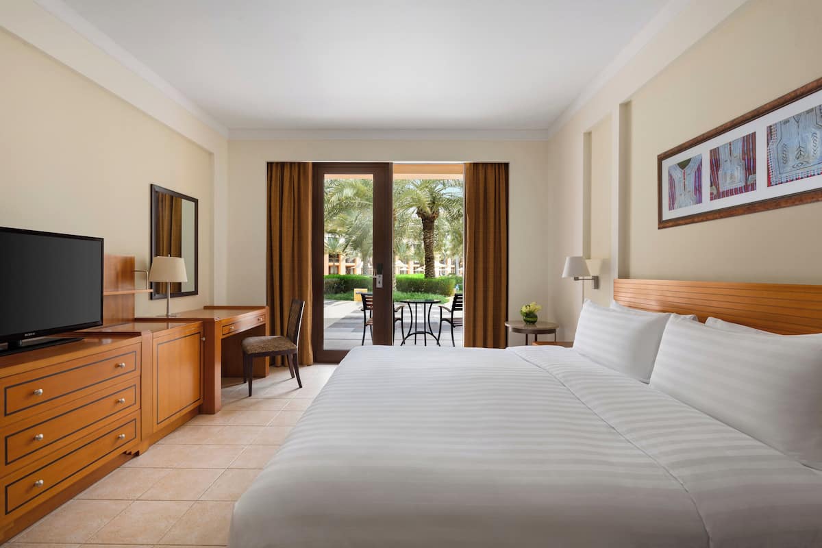 A hotel room with a large bed, a desk with a television, a chair, and a view of the outdoors.
