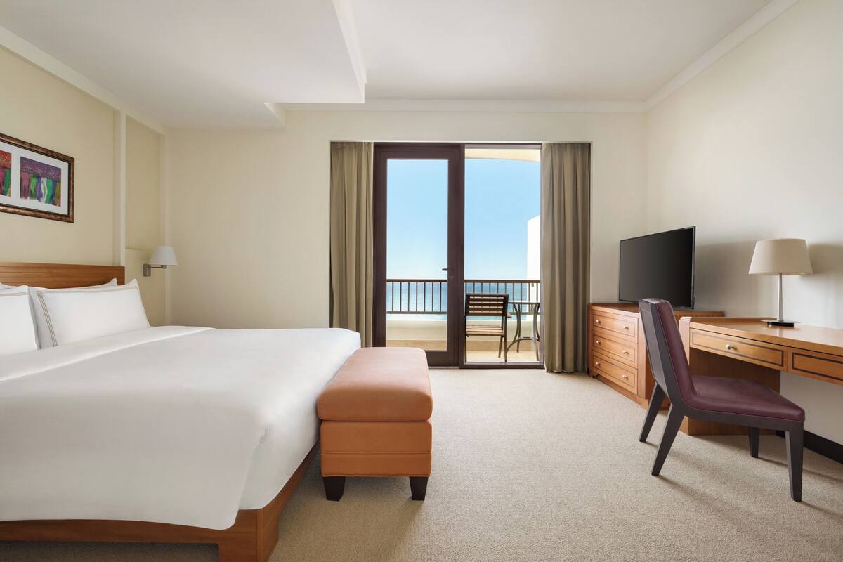 A hotel room with a bed, a desk, a chair, a television, and a balcony with a view.