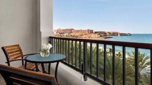 Un balcon avec une table et des chaises, offrant une vue sur la côte, avec des bâtiments et des palmiers.