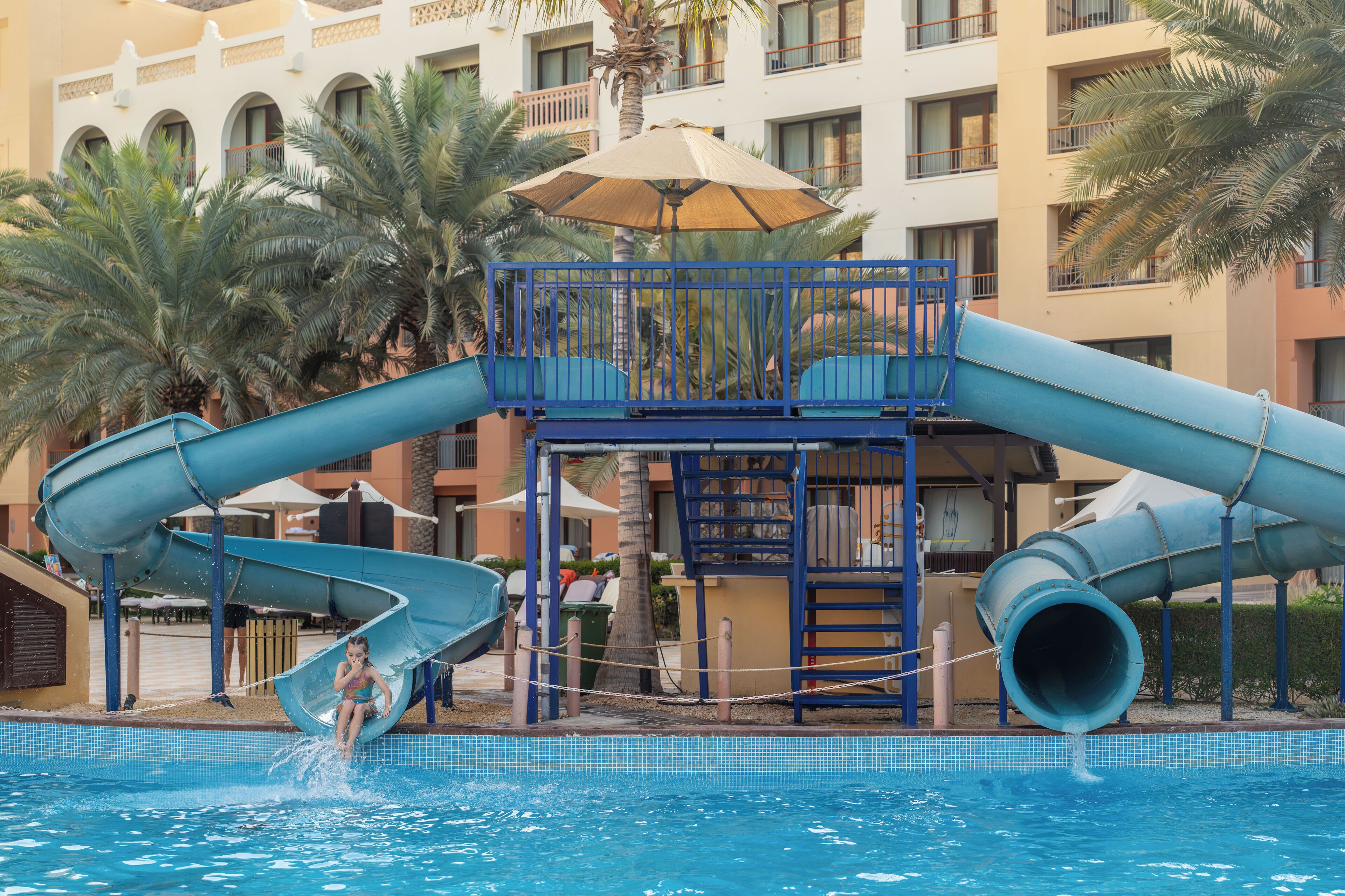 A water park with slides and a pool, surrounded by palm trees and a building with balconies.
