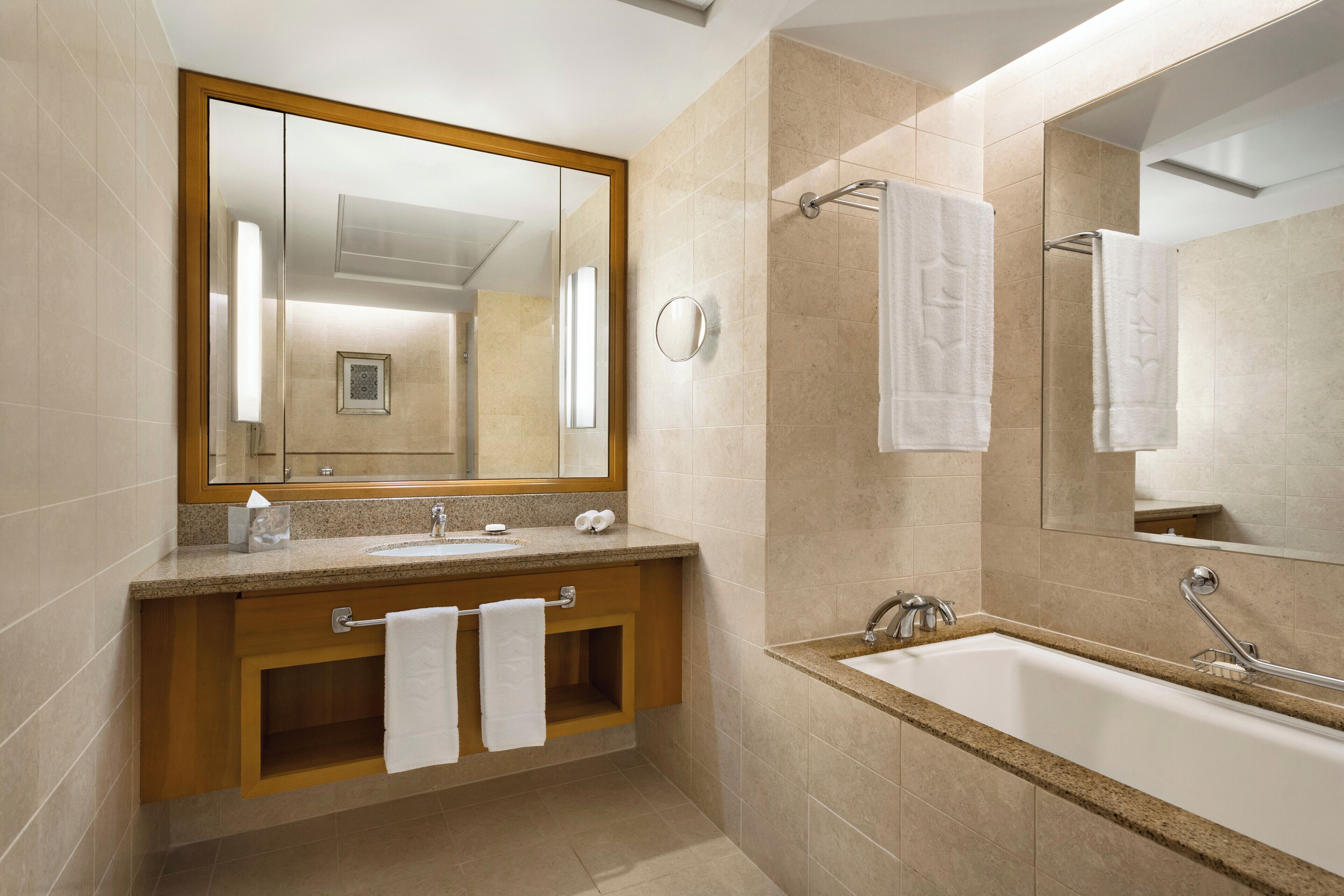 A modern bathroom with a large mirror, a bathtub, and a vanity with a sink and towel rack.