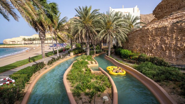 Un parc aquatique avec une piscine, des palmiers et une plage.