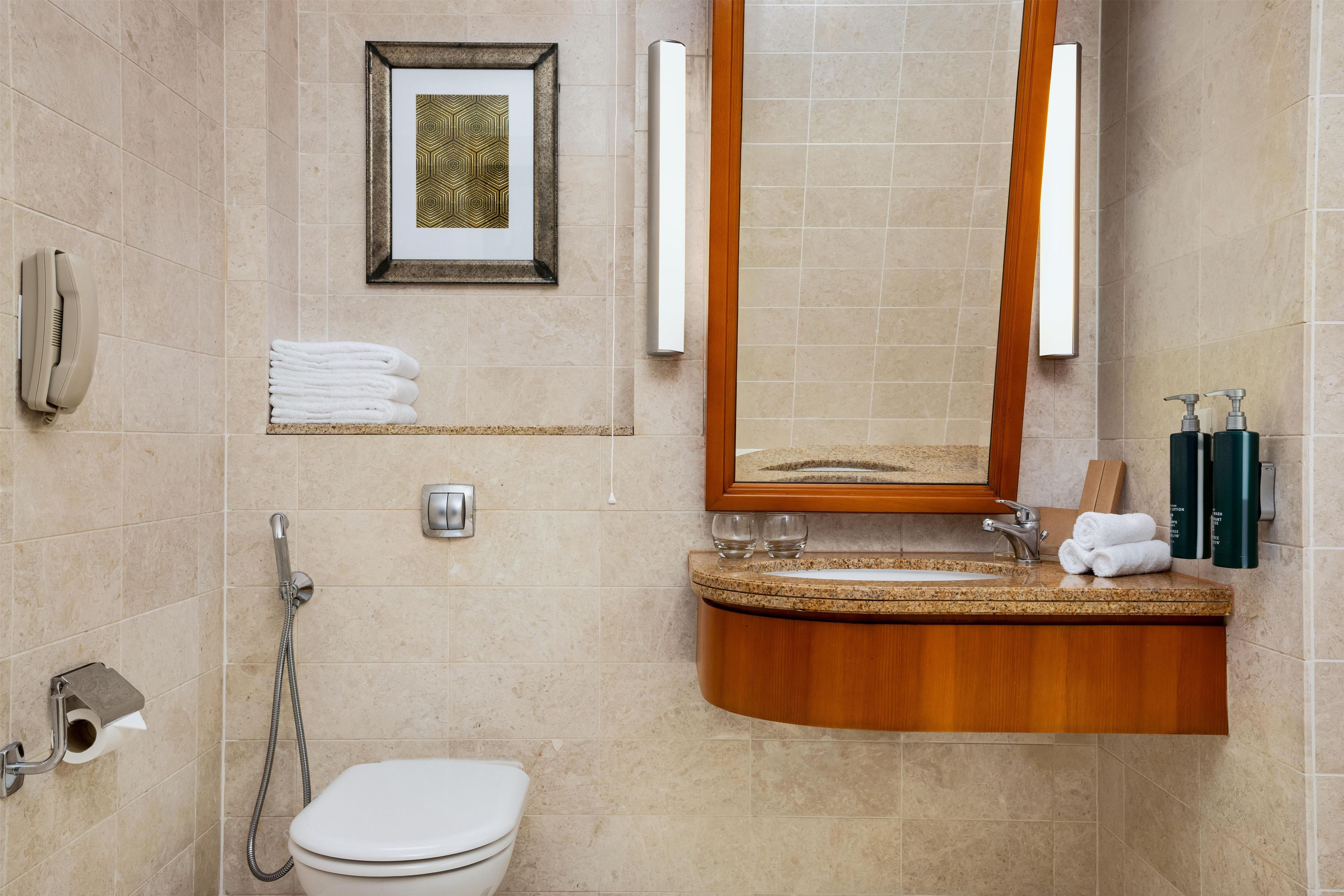 Un baño con inodoro, lavamanos, espejo, una obra de arte enmarcada y un perchero para toallas.
