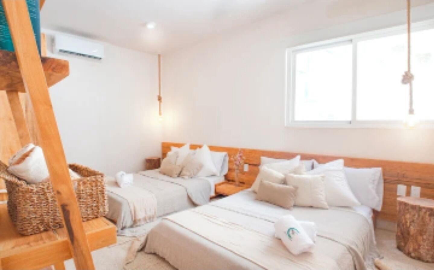 A hotel room with two beds, a wooden headboard, a window with natural light, and a hanging light fixture.