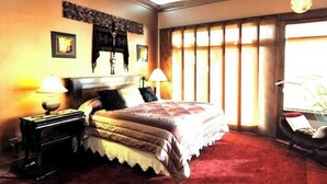 Une chambre d’hôtel avec un grand lit, deux tables de chevet avec des lampes, une cheminée et une grande fenêtre avec des rideaux.
