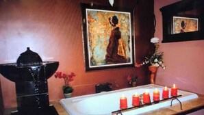 Une salle de bain avec une baignoire, une fontaine à eau noire, une rangée de bougies et un tableau accroché au mur.