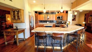A kitchen with a central island, wooden cabinets, a microwave, and a refrigerator. - A touch of the wild west and the loving touch of the pioneer  (Bigfork)