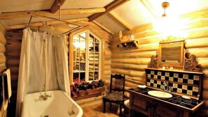 A log cabin bathroom with a bathtub, a sink, and a window with flowers. - A touch of the wild west and the loving touch of the pioneer  (Bigfork)