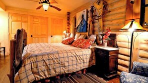 A cozy log cabin-style bedroom with a bed, a nightstand, a lamp, and a chair. - A touch of the wild west and the loving touch of the pioneer  (Bigfork)