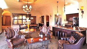 Uma sala de estar espaçosa com uma grande mesa de jantar, cadeiras decoradas, lareira e área de cozinha com eletrodomésticos modernos.