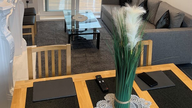 Moderni olohuone, jossa on lasinen sohvapöytä, harmaa sohva sekä ruokailutila, jossa on puinen pöytä ja tuolit.
