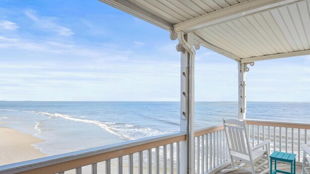Een houten terras met een witte reling met uitzicht op een strand.
