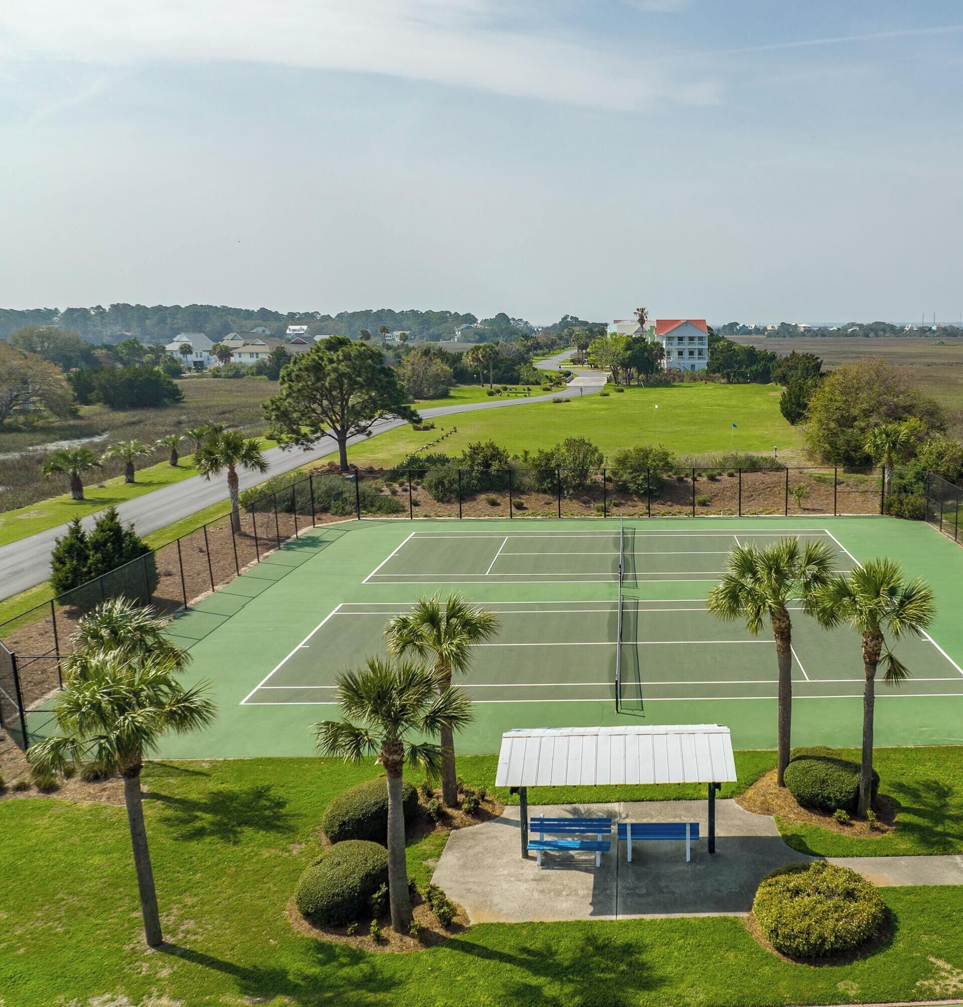 En tennisbana med en paviljong, omgiven av palmer och med utsikt över ett bostadsområde.