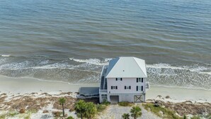 Een huis aan de kust met een metalen dak, gelegen op een zandstrand met uitzicht op zee.