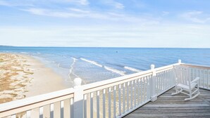 Een houten terras met witte leuningen met uitzicht op een strand.