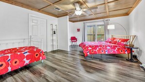 Un dormitorio con dos camas, un ventilador de techo, una ventana con cortinas y una silla roja.