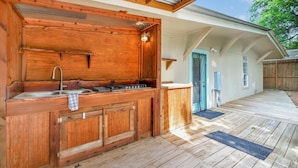 Una cocina exterior de madera con fregadero y estufa, un porche cubierto y una puerta que da a un vestíbulo cubierto.