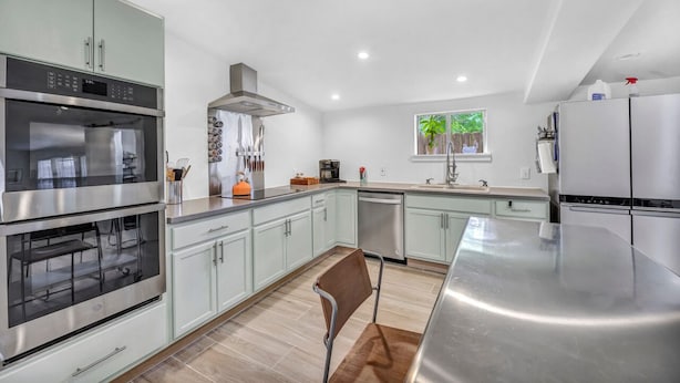 Una cocina moderna con electrodomésticos de acero inoxidable, armarios verde claro y una silla de madera.