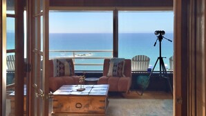 Una habitación acogedora con vista al océano, que presenta un techo de madera, dos sillones, una pequeña mesa y un trípode con una cámara.