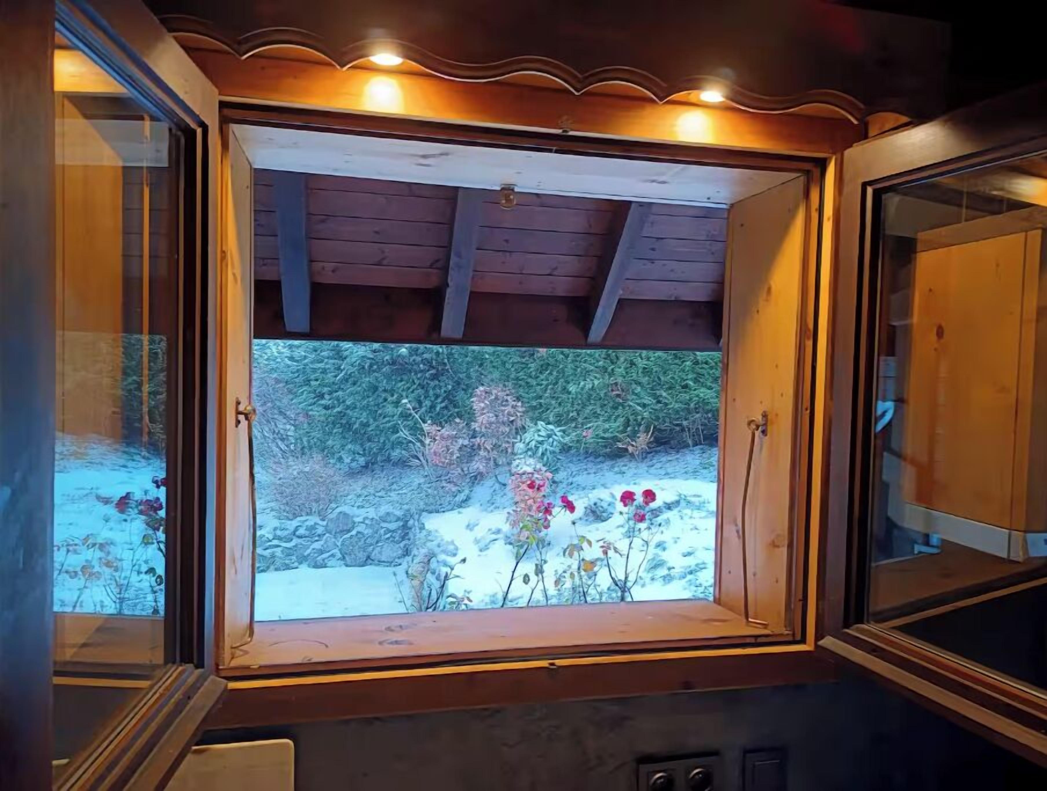 A window with a wooden frame and a view of a garden with flowers and rocks.