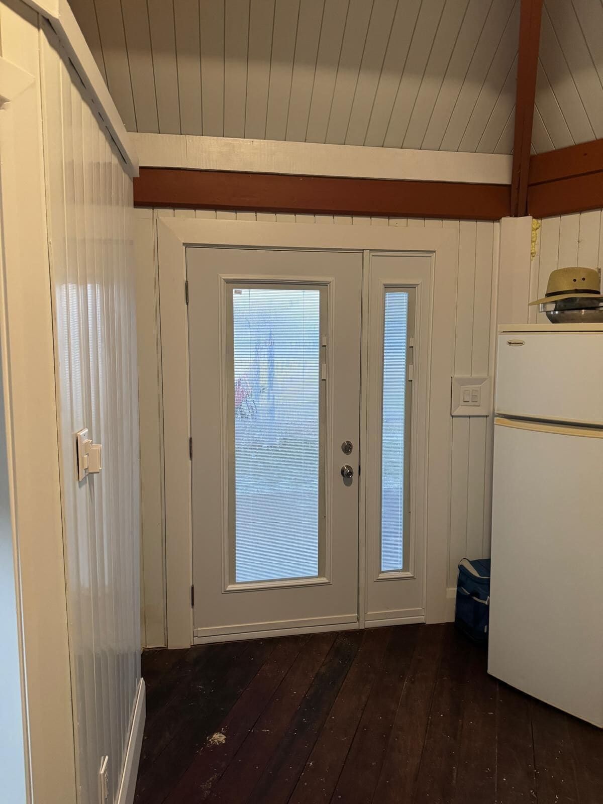 Eine Küche mit zwei weißen Türen, einem Kühlschrank und einem Fenster mit Jalousien.