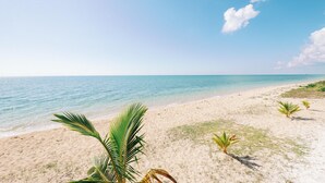 Une plage à l’eau d’un bleu limpide, avec un rivage sablonneux et une végétation clairsemée.