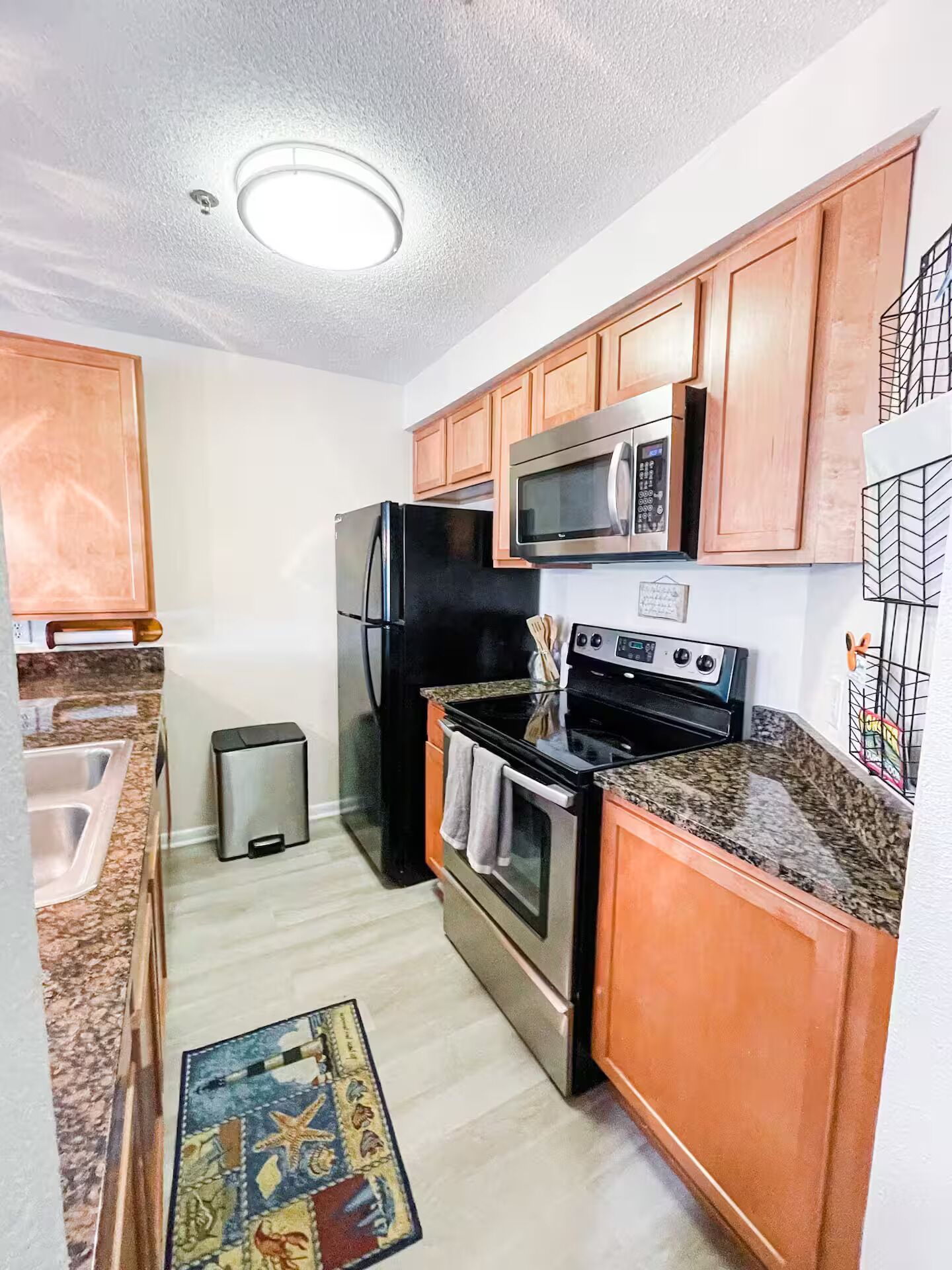 A compact kitchen with wooden cabinets, a stainless steel refrigerator, a microwave, a stove, and a sink.