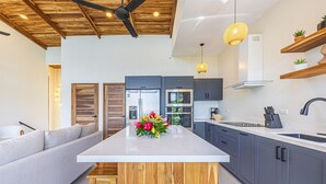 Une cuisine moderne avec des meubles gris, un îlot central blanc et un ventilateur de plafond.