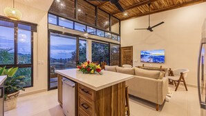 Une cuisine moderne avec un îlot central en bois, de grandes fenêtres et un ventilateur de plafond.