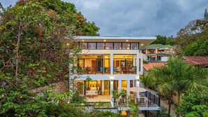 Un hôtel à plusieurs étages doté de balcons, de grandes fenêtres et entouré d’une végétation luxuriante.