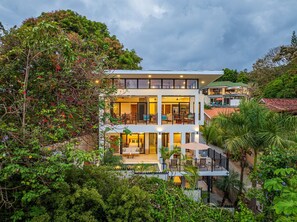 Ein mehrstöckiges Hotel mit Balkonen, großen Fenstern und üppiger Bepflanzung rund um das Anwesen.