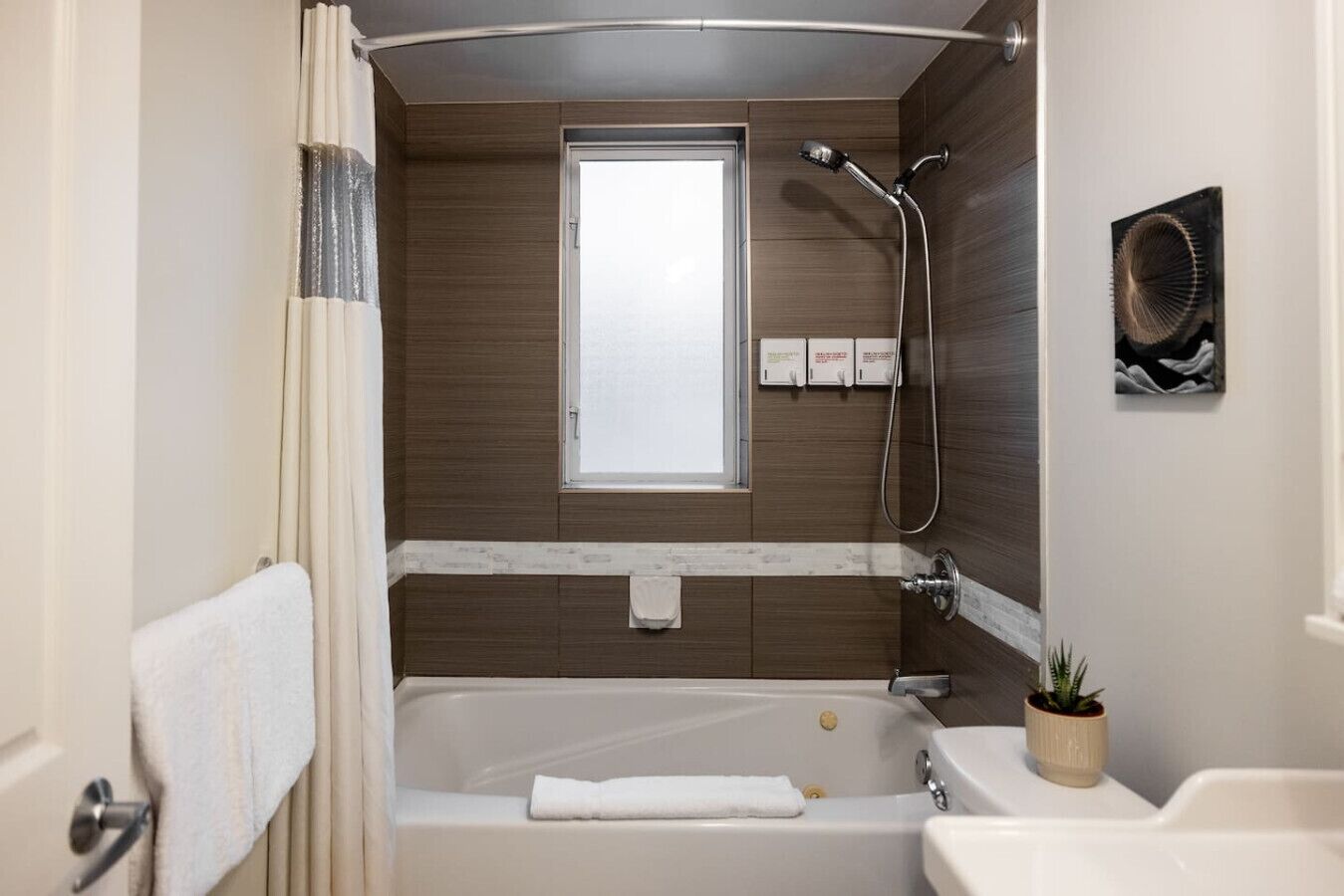 A modern bathroom with a bathtub, shower, and a window.