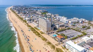 An aerial view of a coastal city with a long beachfront, a large hotel complex, and a marina.