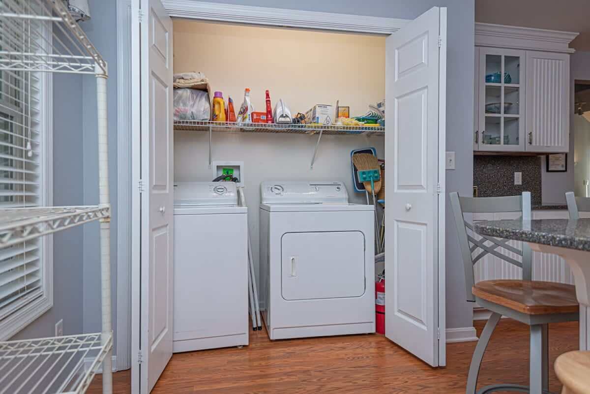 A laundry room with two washing machines, a shelf with cleaning supplies, and a chair.