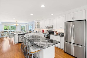 Una cocina moderna con armarios blancos, una isla grande con taburetes de bar, electrodomésticos de acero inoxidable y vistas al exterior.