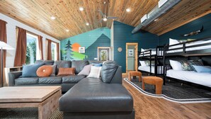 Ein gemütliches Blockhaus-Interieur mit einer großen Couch, einem kleineren Sofa, einem Holztisch und einem Etagenbett.