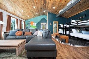 A cozy cabin interior with a large sofa, a smaller couch, a wooden coffee table, and a bunk bed. - Cozy Mountain Hideaway - Hot Tub - Stargazing (Broken Bow)