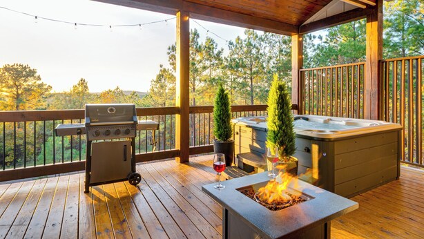 Eine Holzterrasse mit Grill, Whirlpool und Feuerstelle.