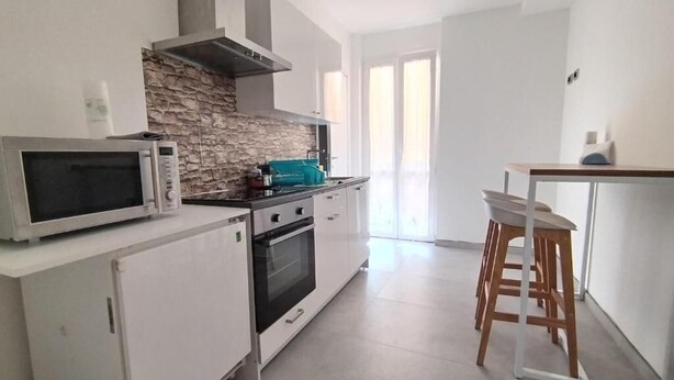 Una cocina moderna con armarios blancos, un protector contra salpicaduras de piedra, un microondas, un horno y una encimera verde azulado.