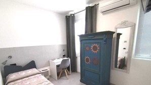 Un dormitorio con cama, escritorio, silla, armario y ventana con cortinas.