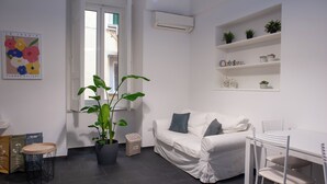 A modern, minimalist living room with a white sofa, a dining table, and a potted plant. - San Liborio bed and breakfast (Naples)