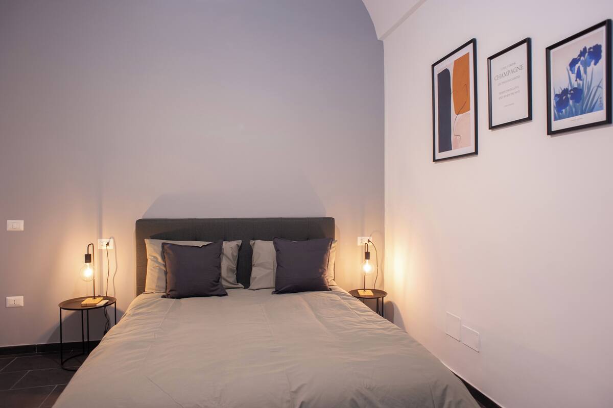 A neatly made bed with a headboard, two bedside tables with lamps, and three framed pictures on the wall.