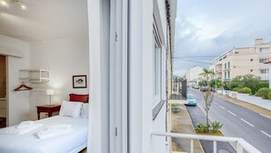 Habitación de hotel con cama, mesita de noche, lámpara y vista a la calle y edificios.