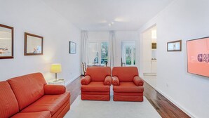 Una sala de estar moderna con un sofá, dos sillones, un televisor y cuadros enmarcados en la pared.