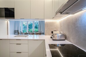 A modern kitchen with a central island, built-in appliances, and a view of greenery outside. - GuestReady- Casa do Visconde (Ponta Delgada)