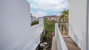 Un patio estrecho con paredes blancas, una terraza de madera y una pequeña mesa con una tetera.