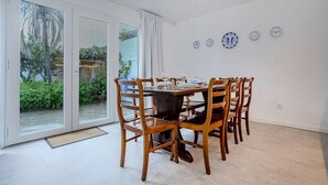 Comedor con mesa dispuesta para seis personas, sillas de madera y vistas a un jardín a través de puertas de vidrio.