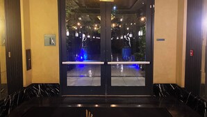 Un vestíbulo interior con un felpudo negro que muestra un logotipo, un accesorio de iluminación en el techo y una señal de salida.